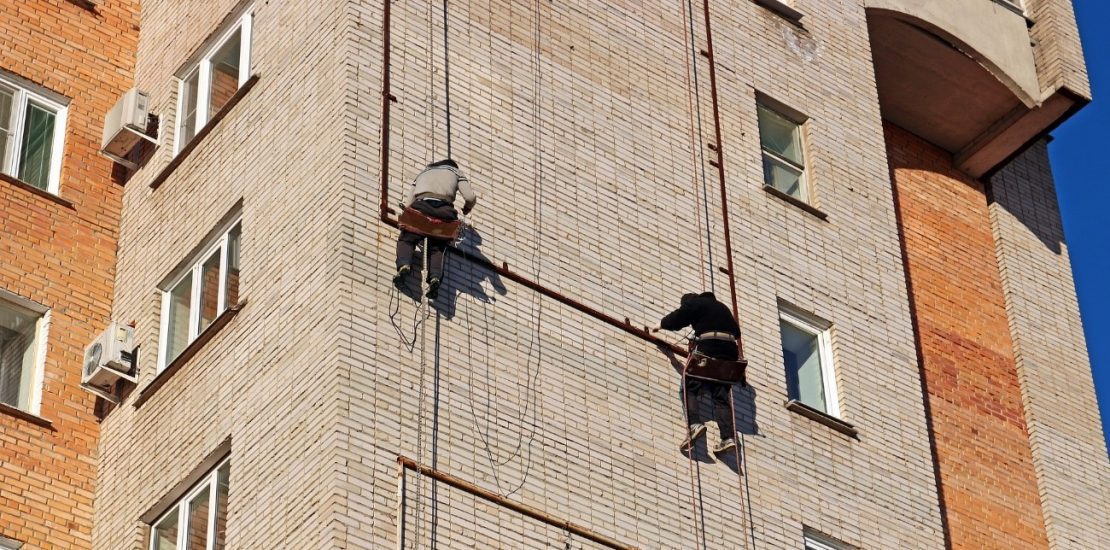 Dois homens trabalhando na parte externa de prédio usando cinto tipo paraquedista para trabalho em altura